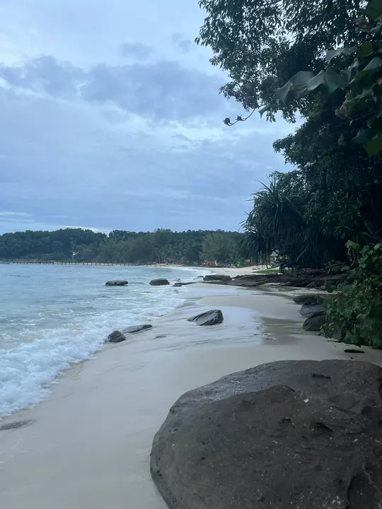 Small waves washing around rocks on a quiet tropical beach beneath a cloudy blue evening sky.
