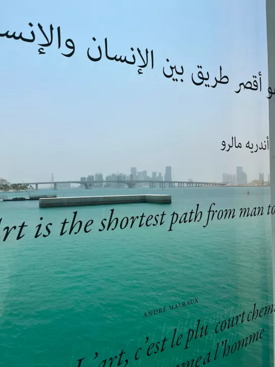 André Malraux’s quotation in three languages across a window overlooking turquoise water and the Abu Dhabi skyline.