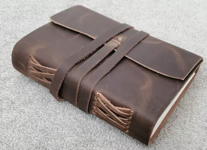 A thick brown leather journal with wraparound straps.
