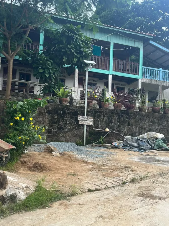 A rustic turquoise building among tropical plants, with a sign advertising motorbike hire at Coconut Beach.