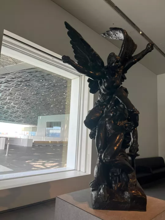A dark winged figurative sculpture beside a window beneath the museum’s patterned dome.